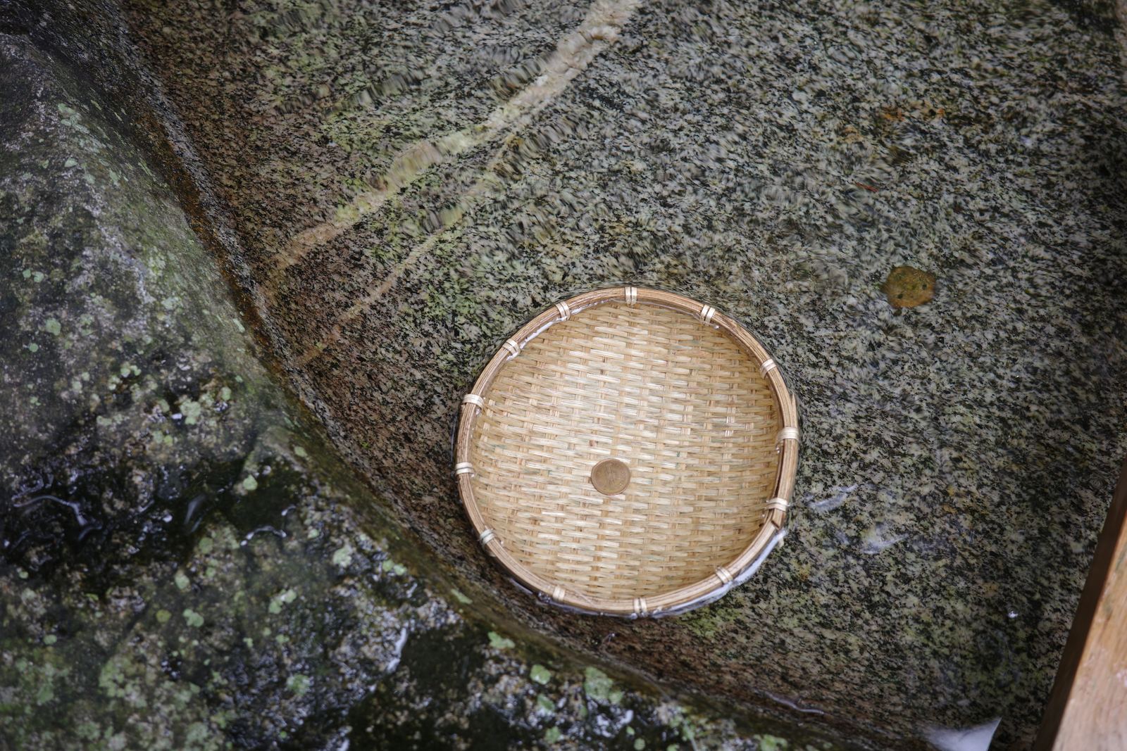 湧き水を張った石の水場に置かれた竹のカゴ。中に10円玉が1枚だけ入っている