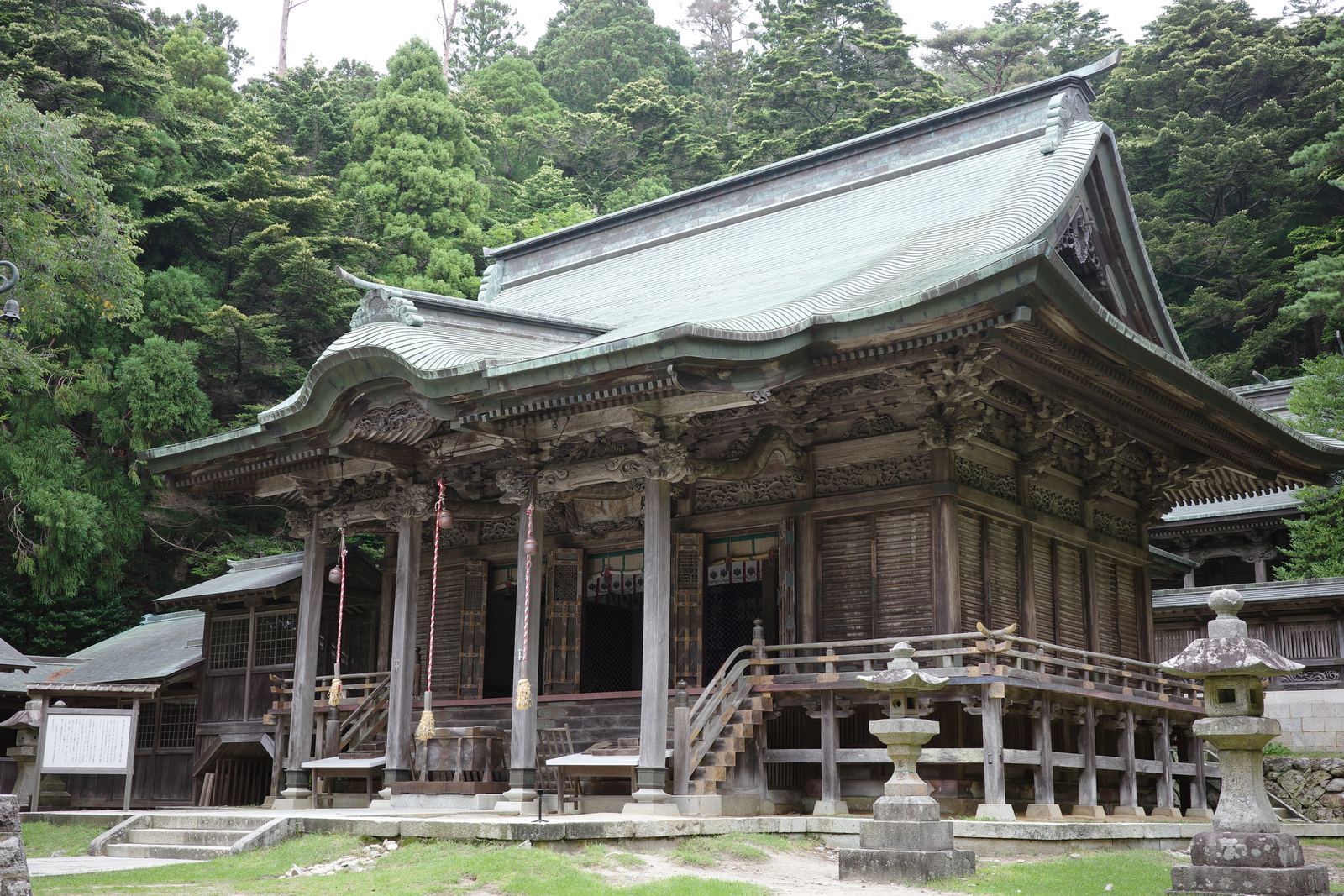 緑青色の屋根と細かな彫刻が施された金華山黄金山神社の本殿。背後は深い森