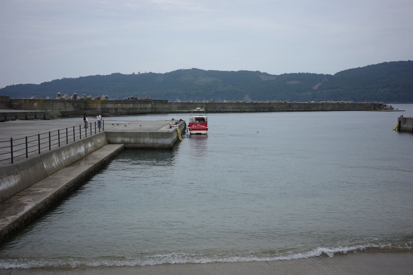 金華山港に着岸した赤い海上タクシー「シードリーム」。奥に防波堤と対岸の山並み、手前に砂浜
