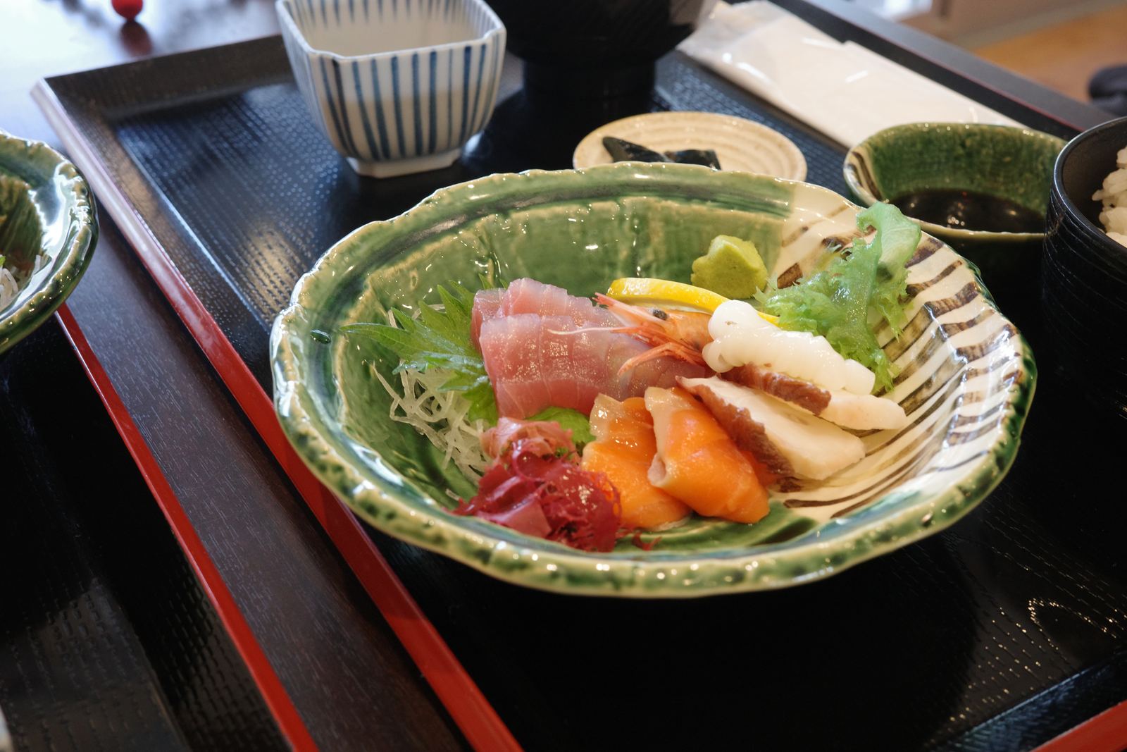 黒い膳に載った海鮮定食。緑の器に刺身が盛られ、味噌汁とご飯が添えられている