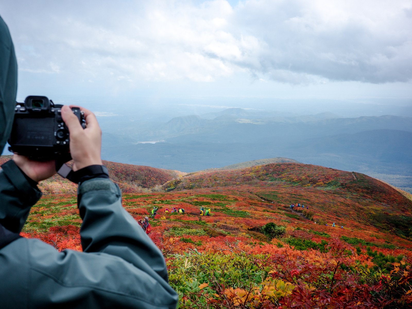 紅葉に覆われた山の斜面を前に、カメラを構えて撮影する登山者