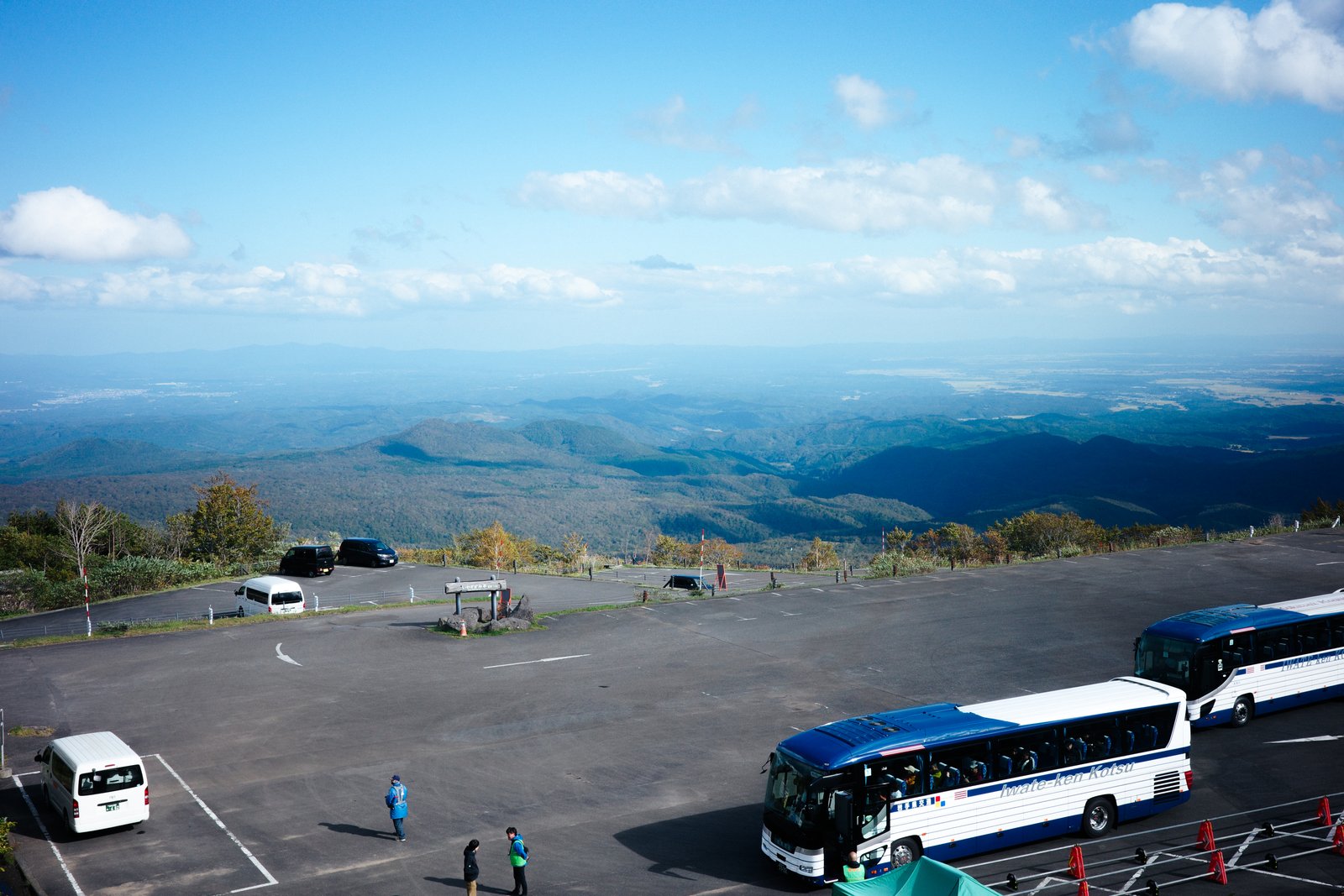 下山後のいわかがみ平の駐車場に停まるシャトルバス。青空の下、遠くの平地と山並みが見える