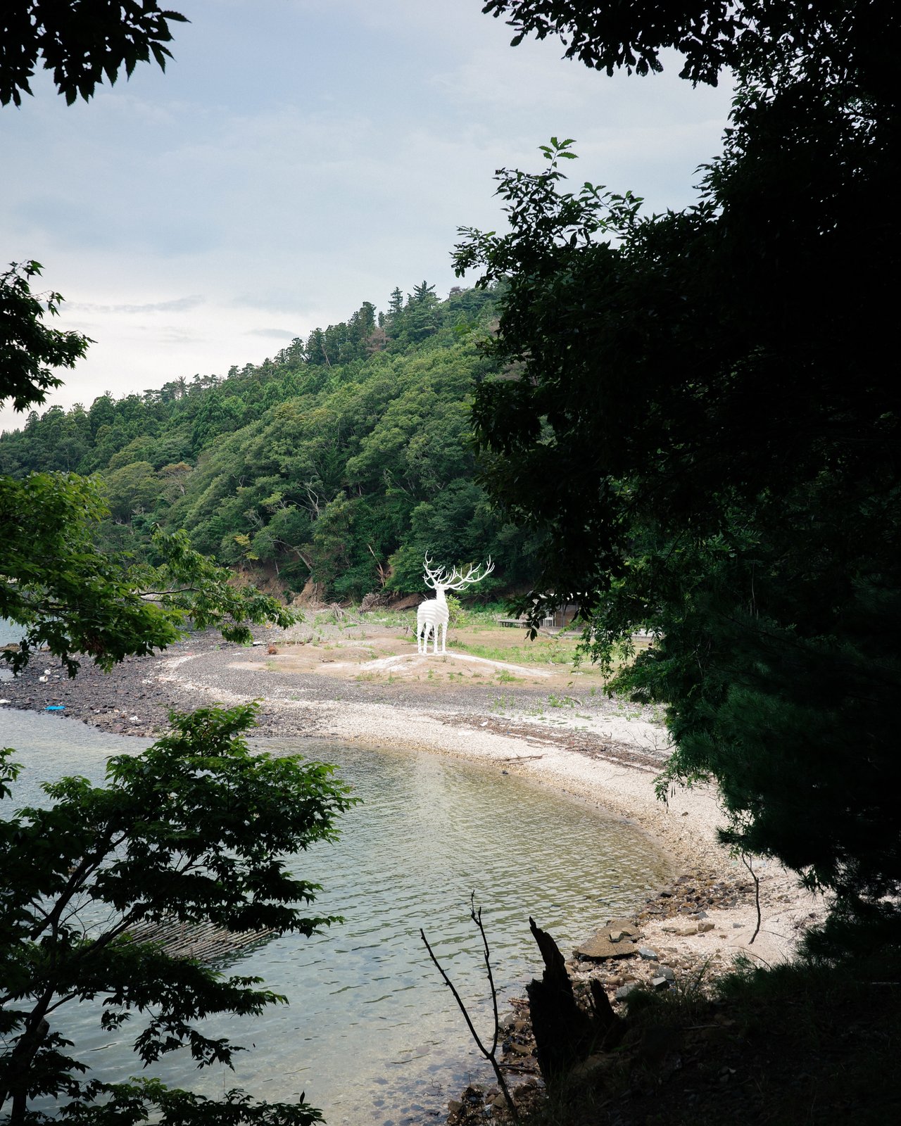 木の枝ごしに見える入り江。対岸の白い浜に、小さく白い鹿の彫刻が立っている